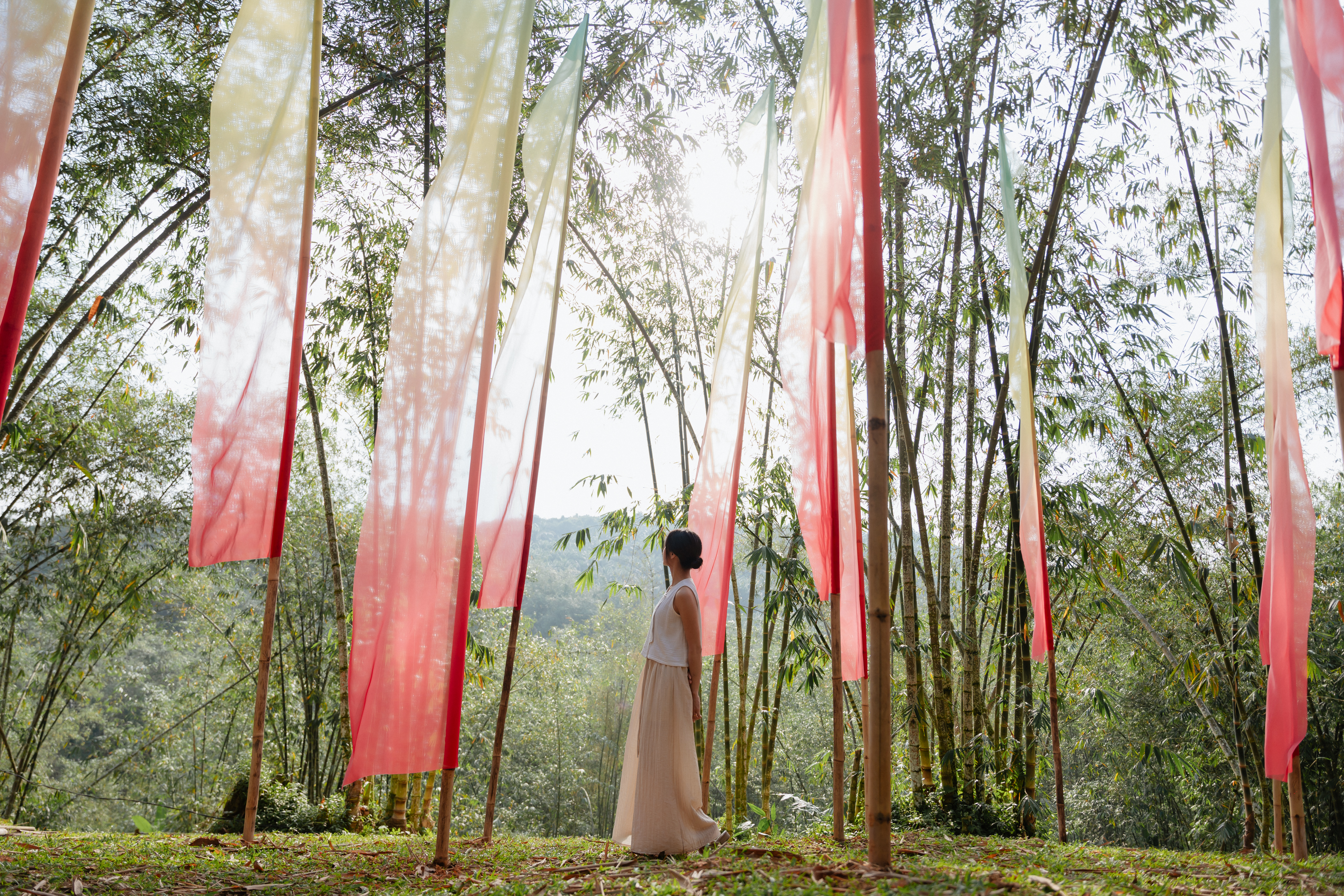 A woman standing in a bamboo grove hung with ceremonial ribbons